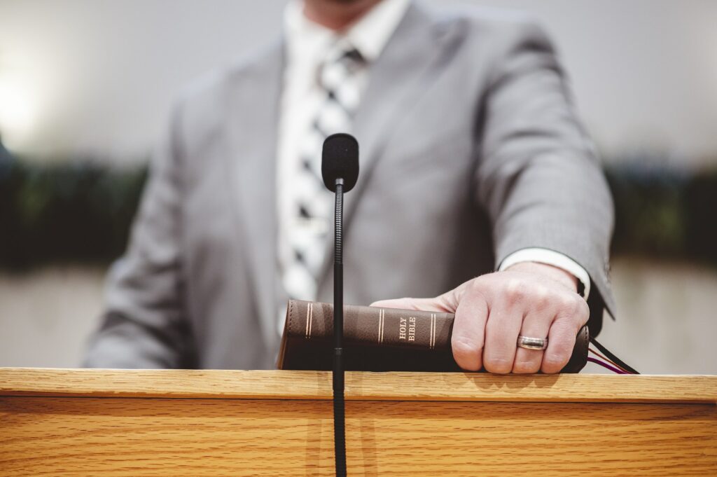 Male in a grey suit preaching words of the Holy Bible at the altar of a church